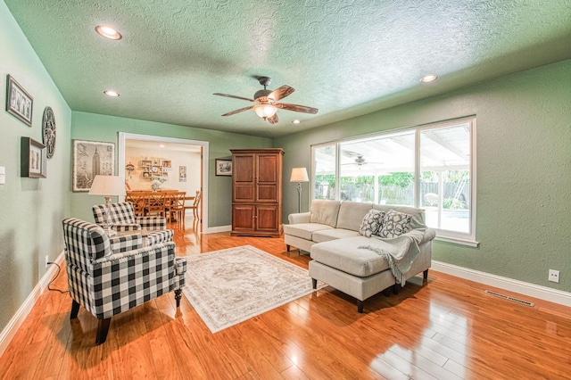 living room featuring a textured ceiling, ceiling fan, and baseboards