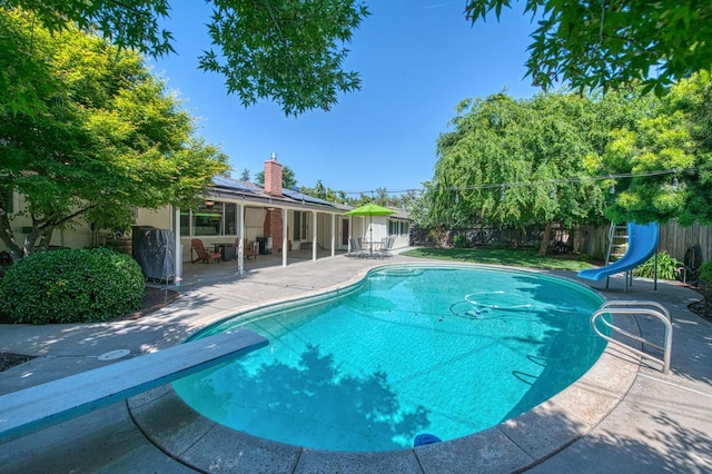 view of pool featuring a diving board, a water slide, a fenced in pool, a fenced backyard, and a patio area