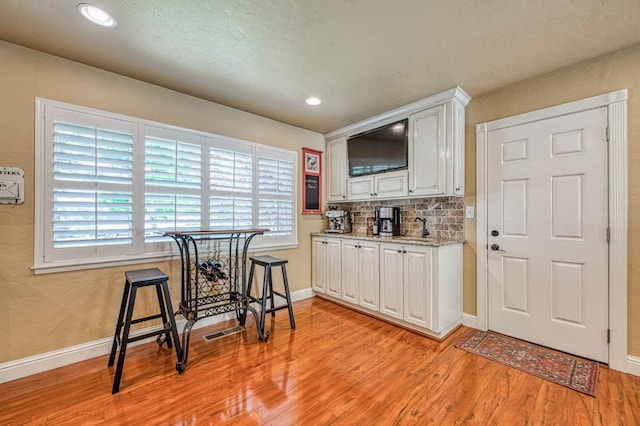 kitchen featuring light wood-style floors, baseboards, decorative backsplash, and white cabinetry
