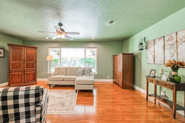 living room featuring light wood-style floors, a textured ceiling, and ceiling fan