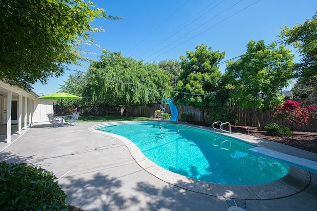 view of swimming pool with a diving board, a fenced in pool, a fenced backyard, a patio, and a water slide