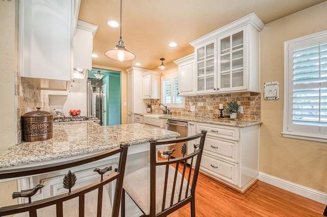kitchen with backsplash, a sink, baseboards, light wood finished floors, and white cabinetry