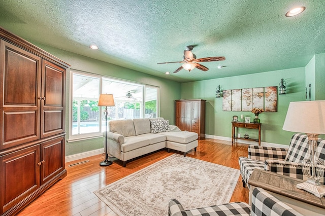 living area with light wood-style floors, baseboards, a ceiling fan, and visible vents
