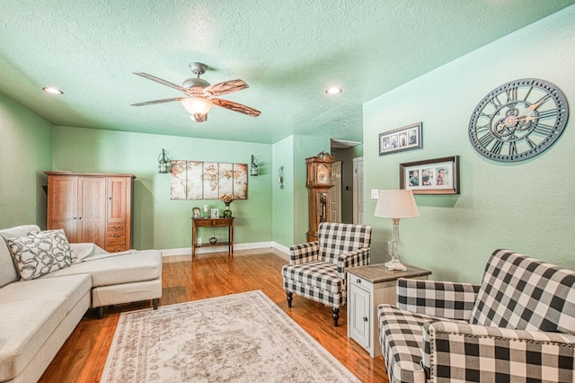 living room featuring baseboards, a textured ceiling, ceiling fan, and wood finished floors