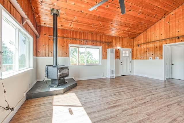 unfurnished living room with vaulted ceiling, light wood-style floors, a wood stove, and a healthy amount of sunlight