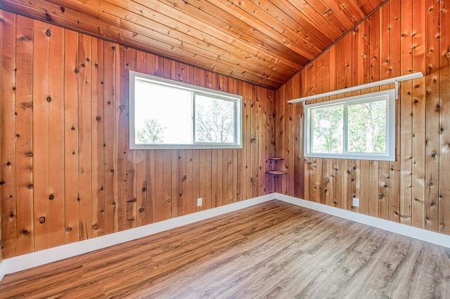 empty room with baseboards, wood walls, wood finished floors, and lofted ceiling
