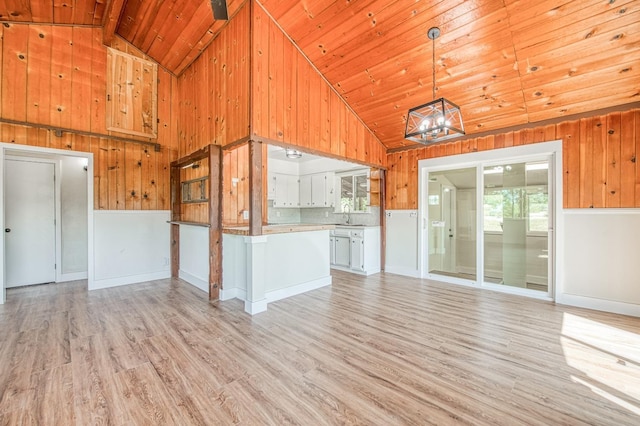 unfurnished living room featuring wooden walls, high vaulted ceiling, wooden ceiling, a sink, and light wood finished floors