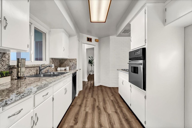 kitchen with dark wood-style flooring, stainless steel oven, black dishwasher, white cabinets, and a sink