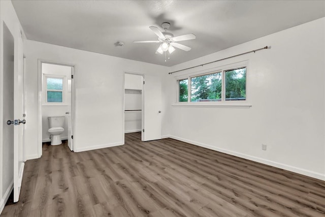 unfurnished bedroom featuring a walk in closet, wood finished floors, baseboards, a closet, and connected bathroom