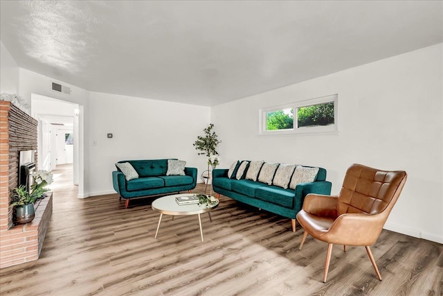 living area featuring baseboards, a brick fireplace, wood finished floors, and visible vents