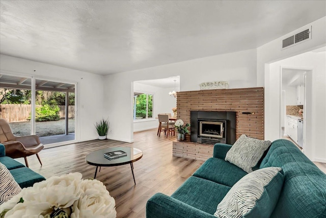 living area featuring a notable chandelier, light wood finished floors, a brick fireplace, baseboards, and visible vents