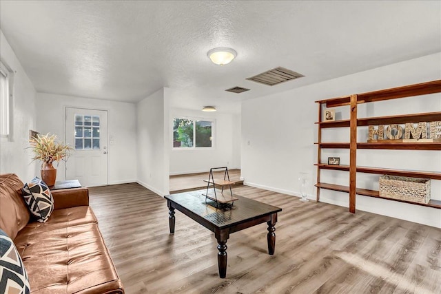 living room featuring baseboards, a textured ceiling, visible vents, and wood finished floors