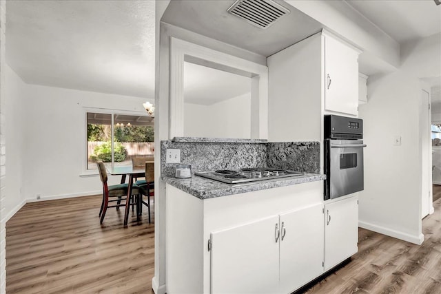 kitchen featuring visible vents, light wood-style floors, stainless steel oven, white cabinetry, and stovetop