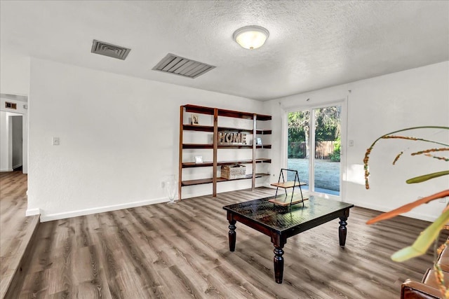 sitting room with a textured ceiling, baseboards, wood finished floors, and visible vents