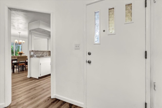 foyer entrance with baseboards, wood finished floors, and a chandelier