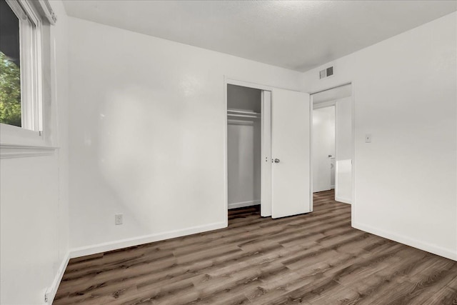 unfurnished bedroom with visible vents, baseboards, wood finished floors, and a closet