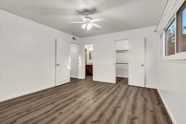unfurnished bedroom featuring visible vents, baseboards, a walk in closet, and wood finished floors