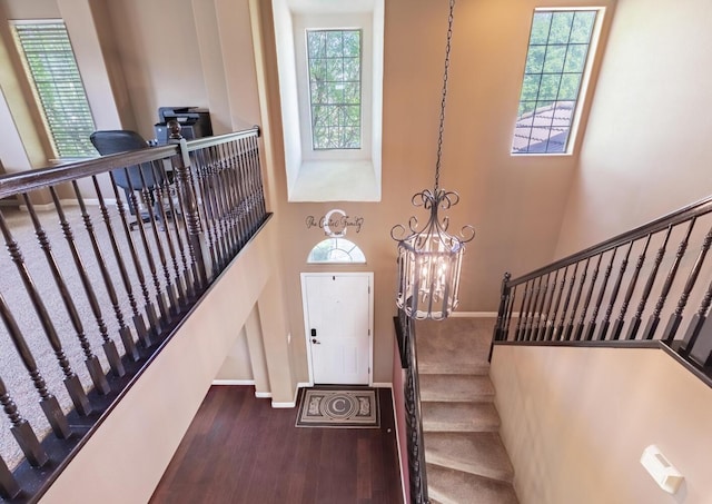 stairs featuring baseboards, a towering ceiling, wood finished floors, and a notable chandelier