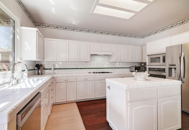 kitchen featuring tile counters, white cabinets, a sink, dark wood finished floors, and stainless steel appliances
