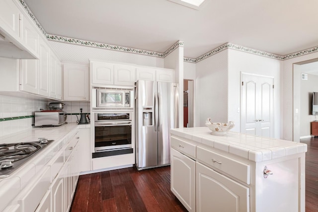kitchen featuring tile countertops, appliances with stainless steel finishes, white cabinetry, and dark wood finished floors