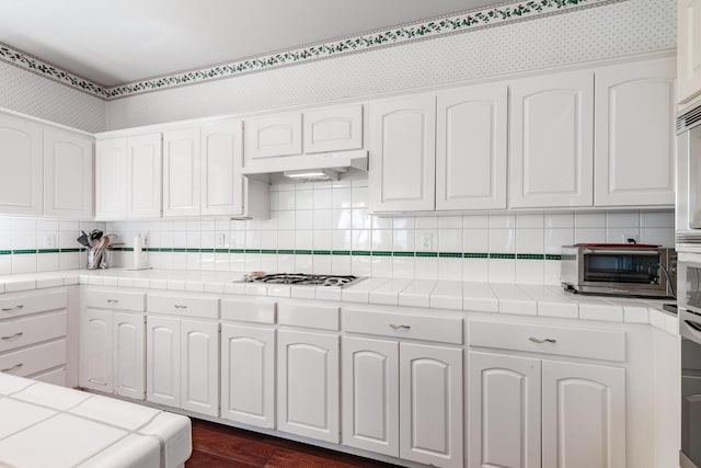 kitchen featuring a toaster, tile counters, gas cooktop, white cabinetry, and tasteful backsplash
