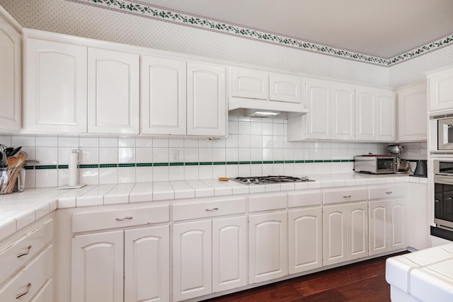 kitchen featuring tile counters, appliances with stainless steel finishes, white cabinetry, and dark wood-type flooring