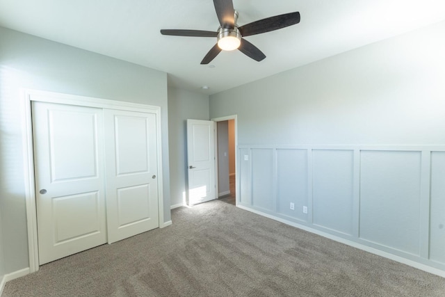 unfurnished bedroom featuring a ceiling fan, carpet floors, a wainscoted wall, a closet, and a decorative wall