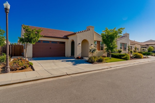 mediterranean / spanish house with an attached garage, stucco siding, a tile roof, and concrete driveway