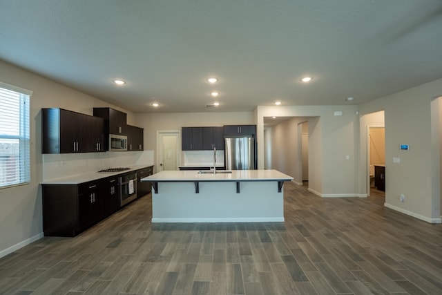 kitchen featuring dark wood-style flooring, a kitchen breakfast bar, light countertops, a sink, and stainless steel appliances