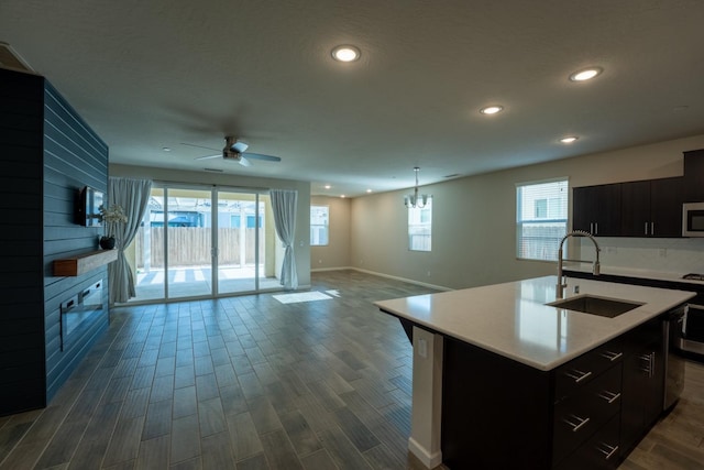 kitchen with dark cabinetry, stainless steel microwave, open floor plan, and a sink