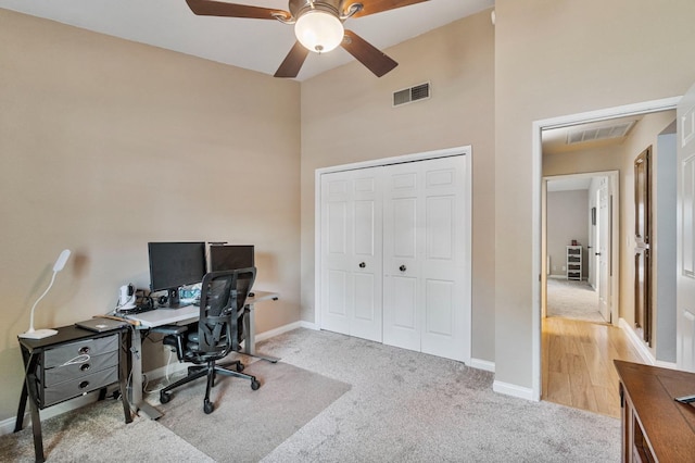 office featuring a ceiling fan, visible vents, baseboards, a high ceiling, and carpet