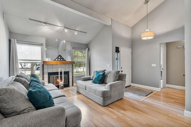 living area featuring a fireplace, wood finished floors, track lighting, baseboards, and high vaulted ceiling