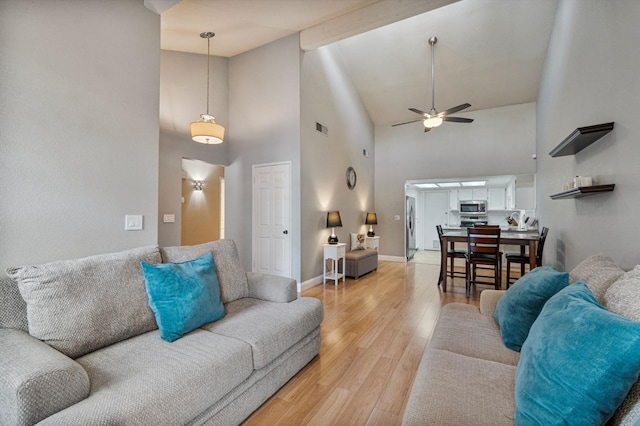 living room with a ceiling fan, visible vents, high vaulted ceiling, baseboards, and light wood-style flooring