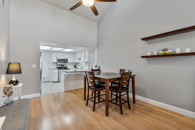 dining area with high vaulted ceiling, baseboards, a ceiling fan, and light wood-type flooring