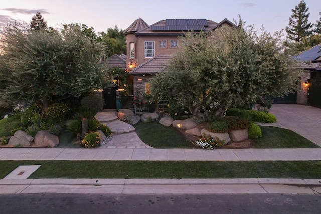 view of front facade featuring roof mounted solar panels, stucco siding, a tile roof, and stone siding