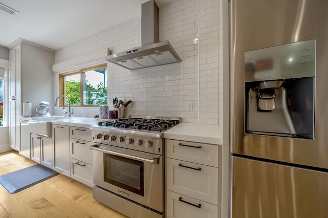 kitchen featuring visible vents, wall chimney range hood, light countertops, backsplash, and stainless steel appliances