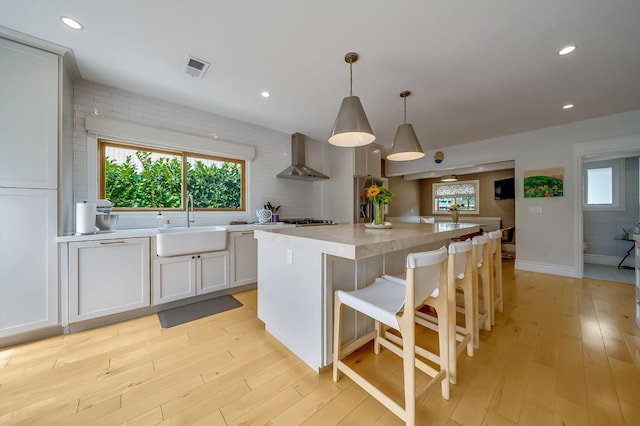 kitchen with visible vents, a center island, a sink, light countertops, and light wood-style flooring