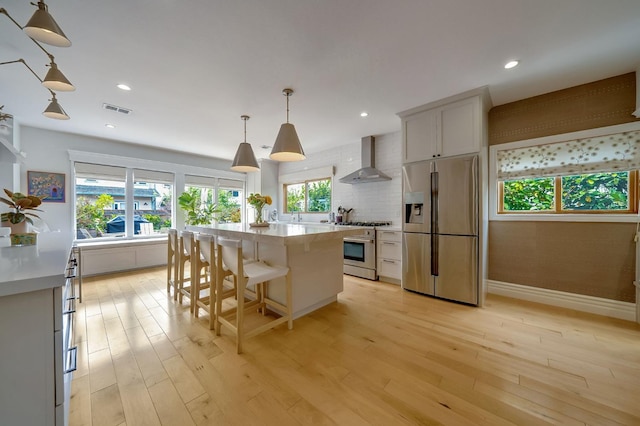 kitchen featuring light countertops, appliances with stainless steel finishes, plenty of natural light, and wall chimney exhaust hood