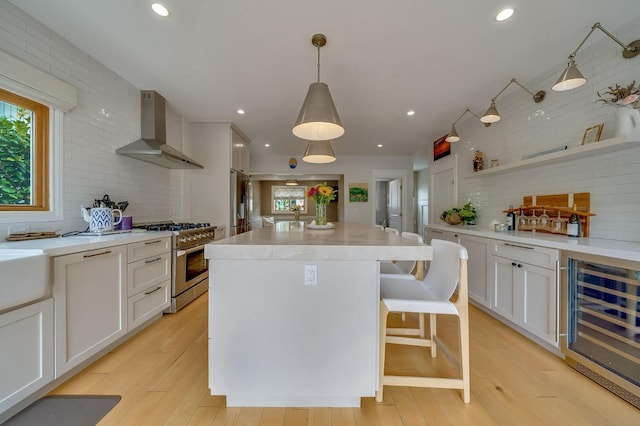 kitchen featuring decorative backsplash, appliances with stainless steel finishes, white cabinets, beverage cooler, and wall chimney exhaust hood