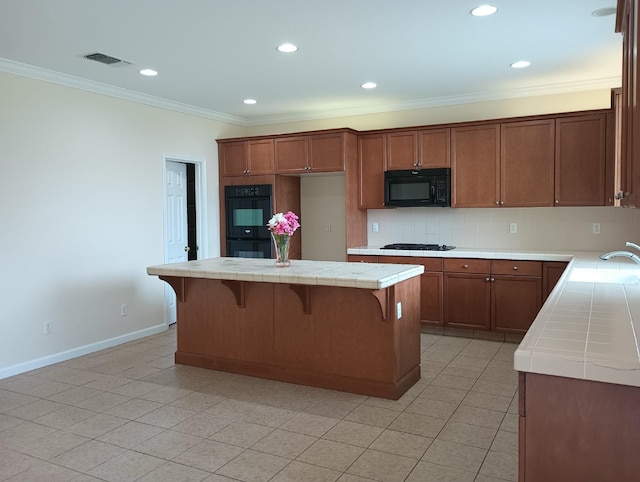 kitchen featuring visible vents, ornamental molding, tile counters, brown cabinets, and black appliances