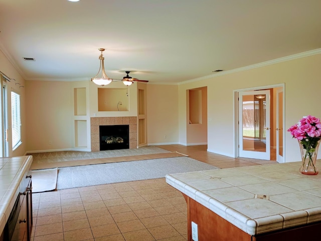 kitchen with ceiling fan, tile countertops, visible vents, crown molding, and a tiled fireplace