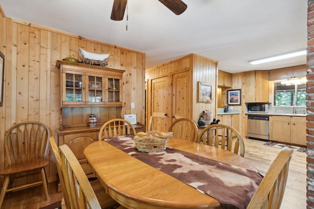 dining room featuring wooden walls, ceiling fan, and light wood-type flooring