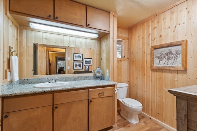 bathroom featuring toilet, wood walls, wood finished floors, and vanity