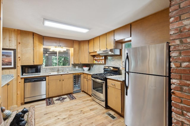 kitchen with appliances with stainless steel finishes, a sink, light wood finished floors, beverage cooler, and under cabinet range hood