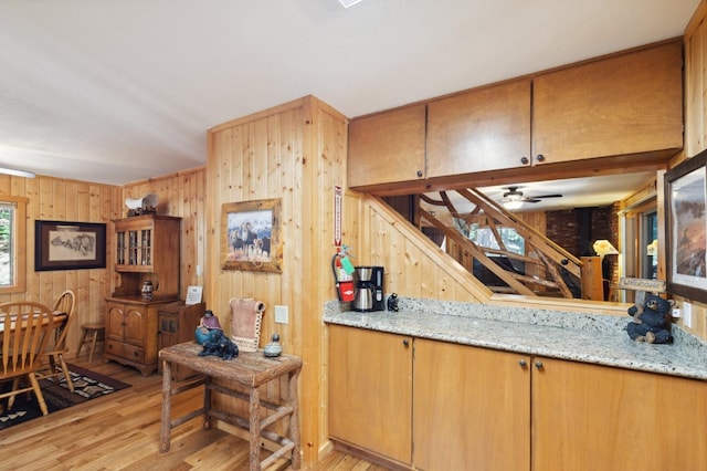 kitchen featuring light wood-style floors, ceiling fan, wooden walls, and light stone countertops