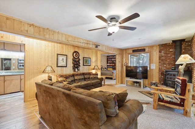 living area with wooden walls, a ceiling fan, a wood stove, and light wood finished floors