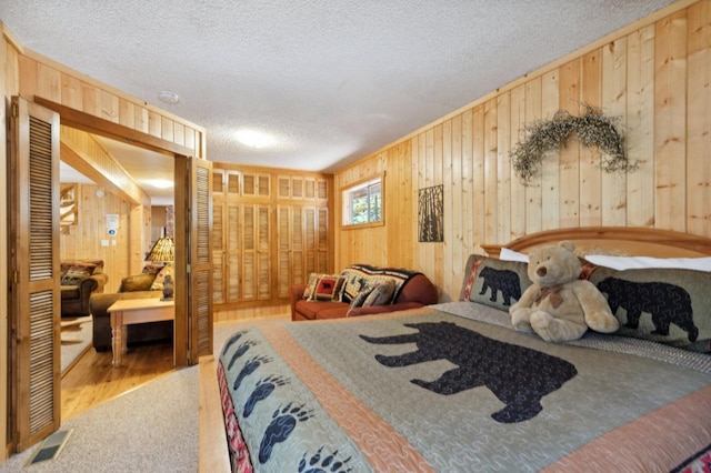 bedroom with visible vents, wood walls, a textured ceiling, and carpet flooring