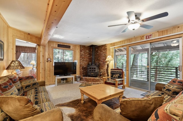 living area with a wood stove, a ceiling fan, wooden walls, and light carpet