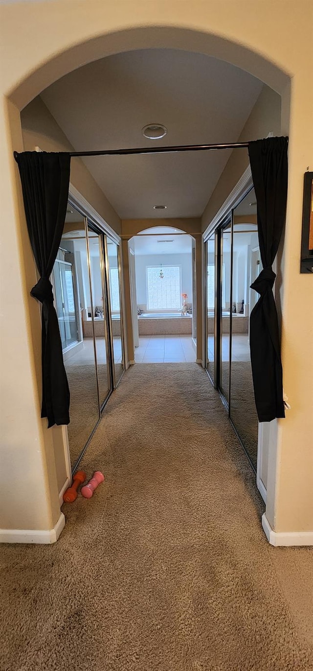 corridor with carpet floors, arched walkways, and baseboards