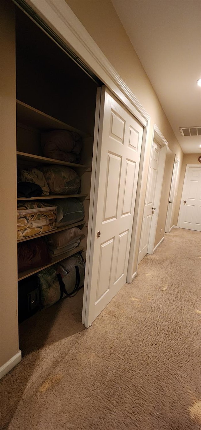 hall with visible vents, baseboards, and light colored carpet